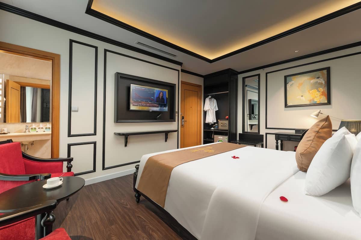 Habitación de hotel con cama, televisor, escritorio y una silla roja.