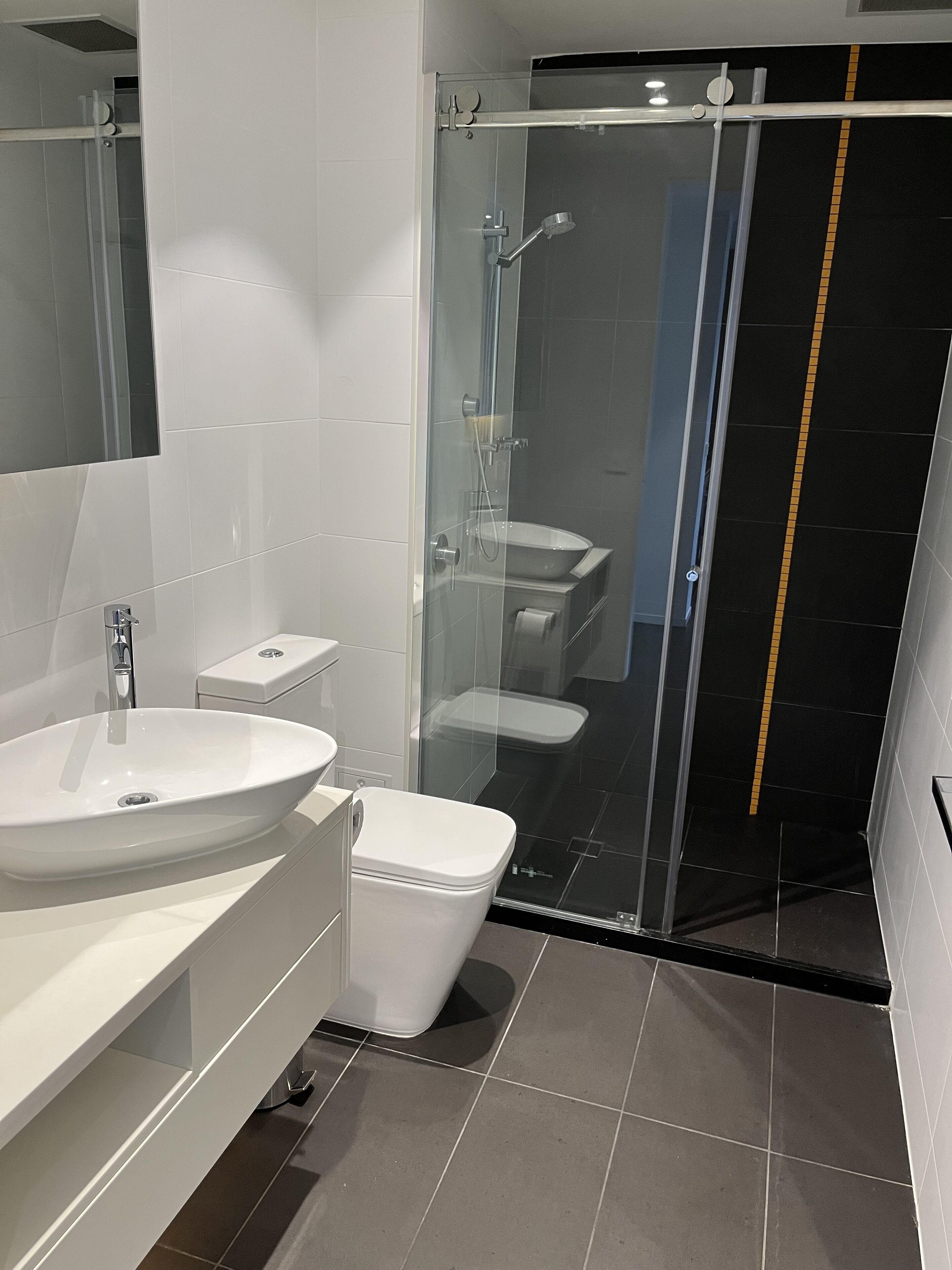 A modern bathroom with a glass-enclosed shower, a white sink, and a toilet.