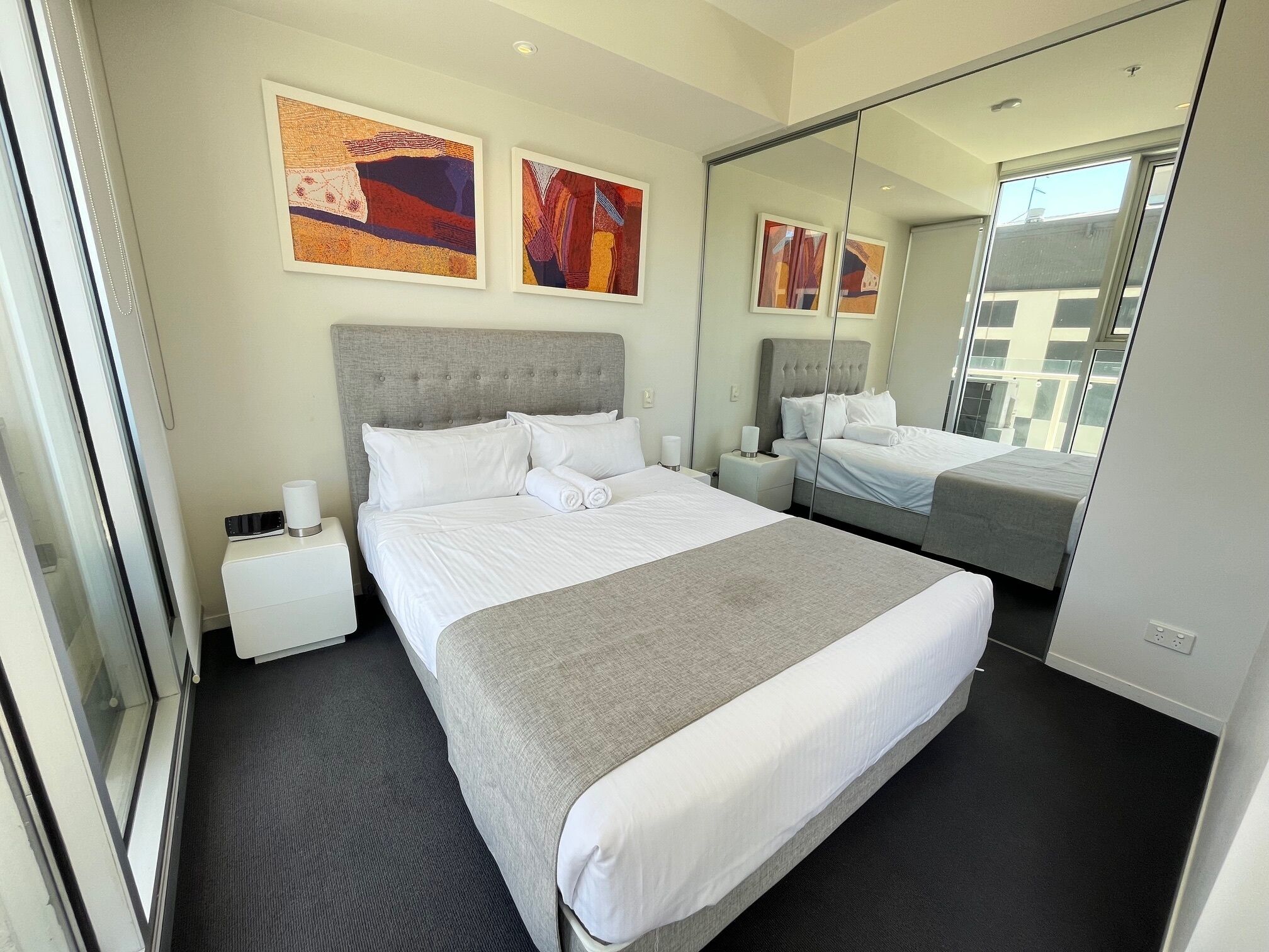 Una camera d'hotel moderna con un letto grande, un comodino, uno specchio e due quadri astratti alle pareti.