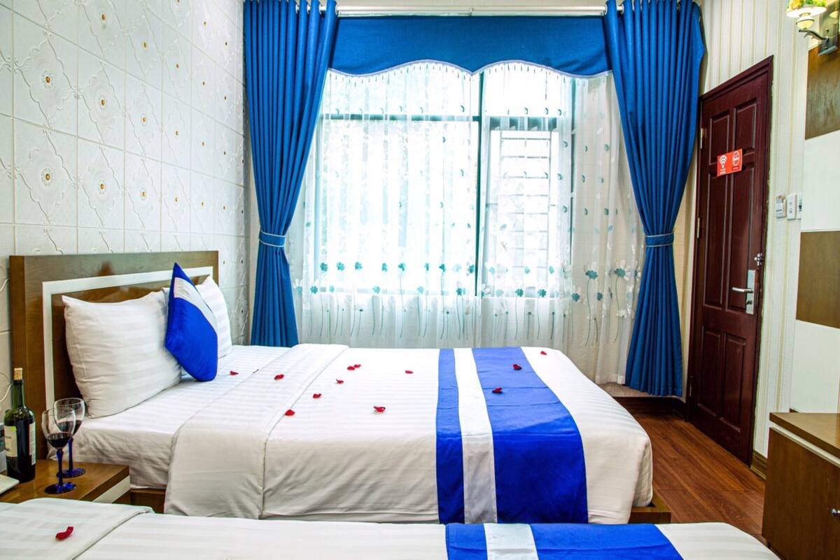 A hotel room with two beds, a wooden headboard, a wooden wardrobe, and a window with blue curtains.