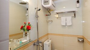 Casa de banho com lavatório branco, sanita e chuveiro. Há uma prateleira de vidro com artigos de higiene e um espelho sobre o lavatório.