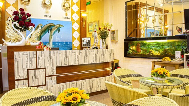 Um saguão de hotel com balcão de recepção, relógios decorativos na parede, um grande aquário e móveis de vime.