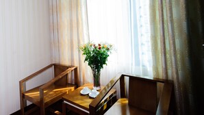Quarto nos fundos com escrivaninha de madeira, cadeira, vaso com flores e janela com cortinas.