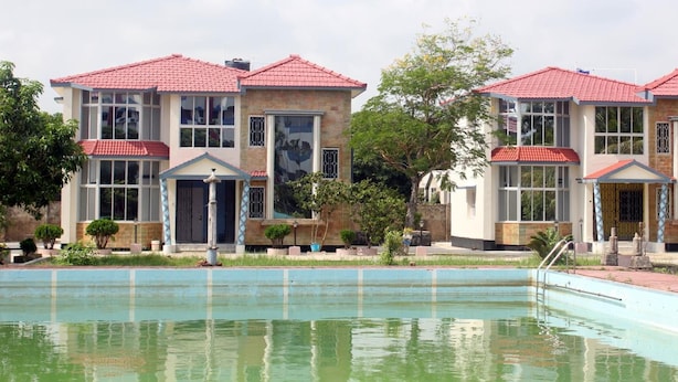 A poolside view of a hotel with multiple buildings, each featuring a red-tiled roof and large windows. - Hotel Deepak (Kakdwip)