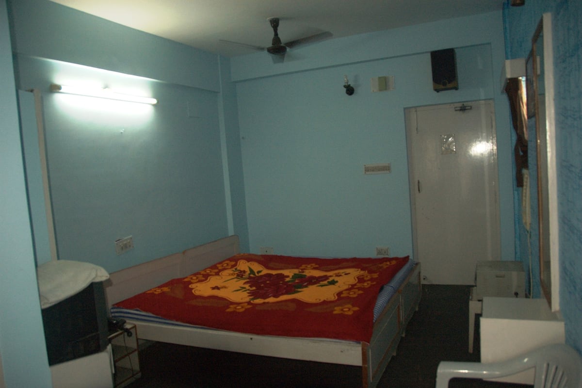 Una habitación con cama, escritorio, silla, ventilador de techo, puerta y lámpara.