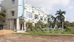 A modern building with a curved glass facade, a playground with swings and slides, and a well-maintained lawn. - Hotel Deepak (Kakdwip)