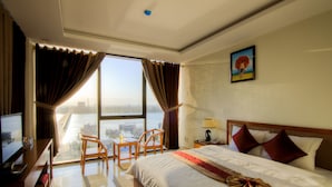 Habitación de hotel con una cama grande, un escritorio con una computadora, una silla y vistas a la ciudad a través de amplios ventanales.