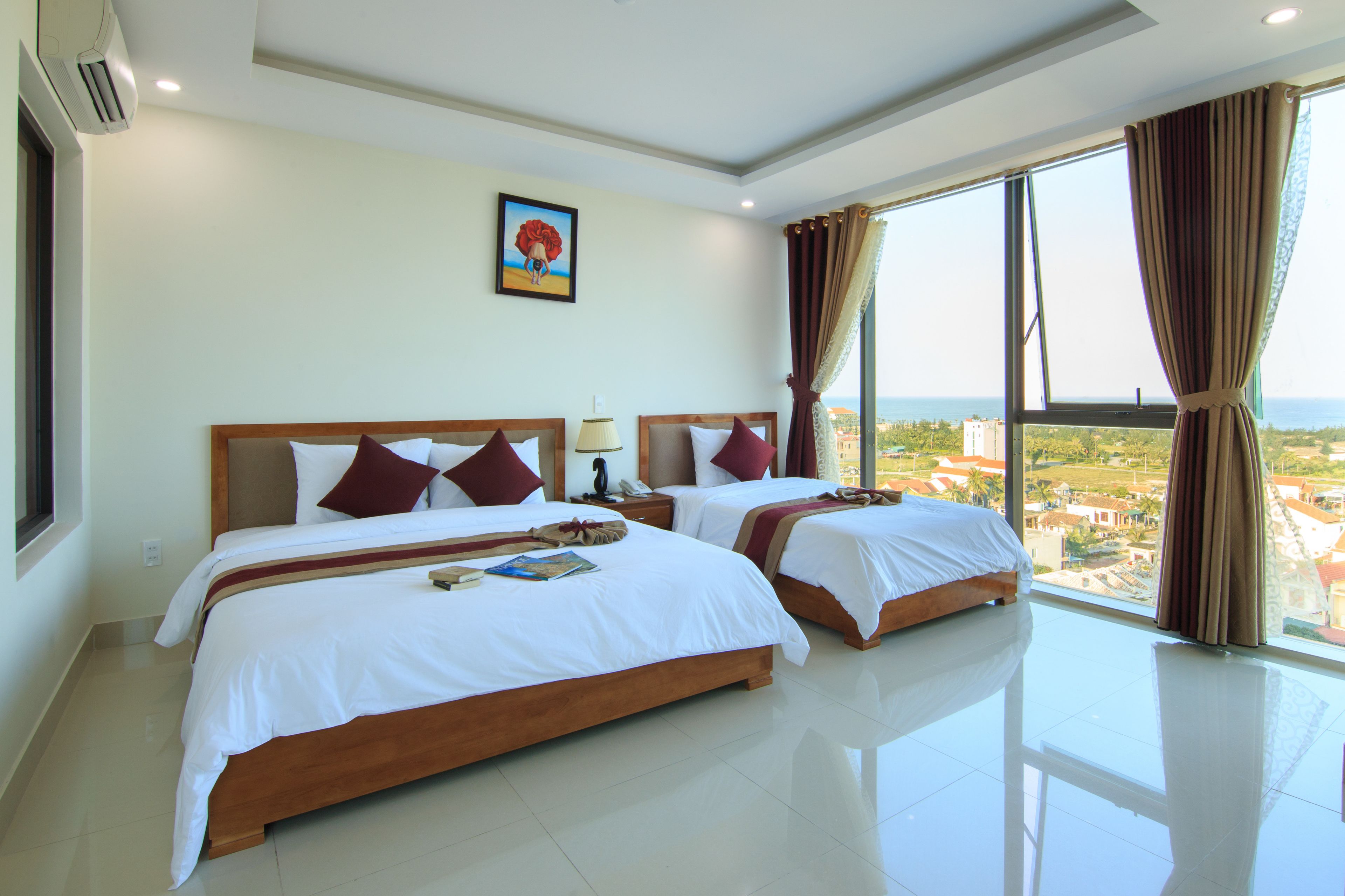 A hotel room with two beds, a large window with curtains, a painting on the wall, and a view of the city.
