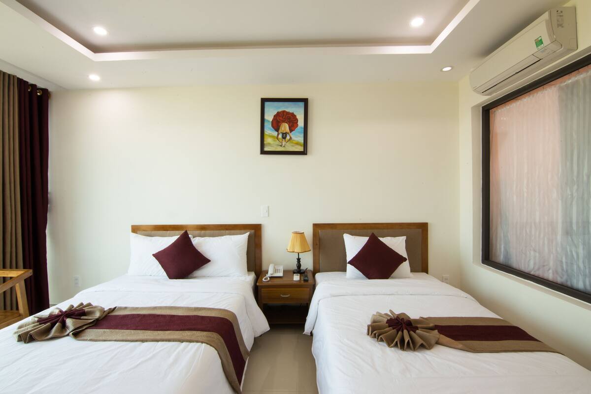 Une chambre d’hôtel avec deux lits, une table de chevet avec une lampe, un tableau au mur et un appareil de climatisation.