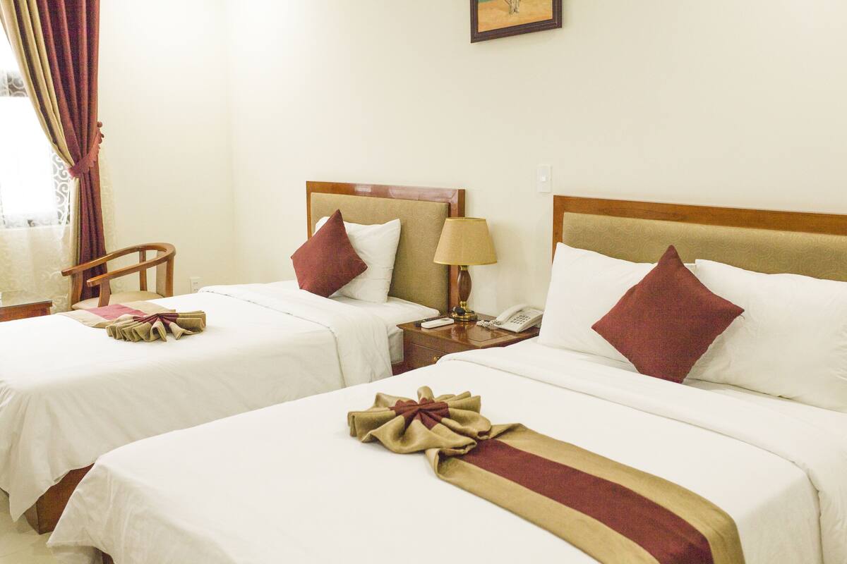 Une chambre d’hôtel avec deux lits, chacun doté de draps blancs et d’oreillers rouges, d’une tête de lit en bois, d’une table de chevet avec une lampe et d’une chaise.