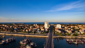 Un pueblo costero con un puente destacado, edificios residenciales y un puerto deportivo con barcos.