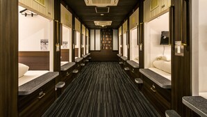 A long, narrow hotel bathroom with individual sinks and mirrors, a central aisle, and a row of bookshelves in the background. - Sejour Inn Capsule (Hiroshima)