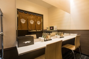 Una habitación de hotel con una mesa larga, sillas, una computadora portátil y un mini bar.