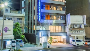 A multi-story hotel with illuminated signage, a parking area, and a street view. - Sejour Inn Capsule (Hiroshima)