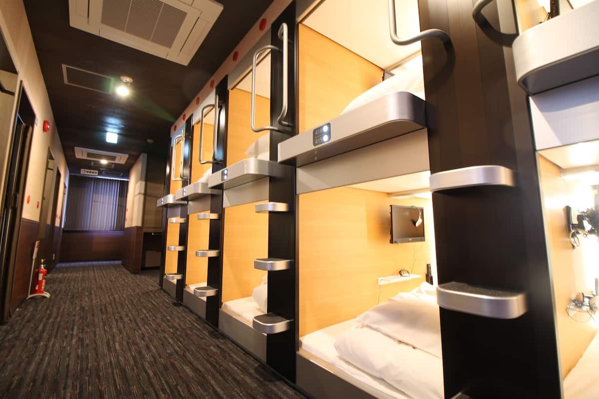 A hotel corridor with bunk beds, a fire extinguisher, and a television mounted on the wall.