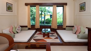 A room with two sofas facing each other, a glass coffee table, and a view of greenery outside. - Camel Valley Resort & Spa (Igatpuri)