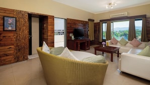 A living room with a sofa, a wicker chair, a TV, and a window with curtains. - Camel Valley Resort & Spa (Igatpuri)