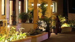A building with a tiled roof, multiple potted plants, and a person standing near the entrance. - Camel Valley Resort & Spa (Igatpuri)