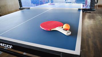 A ping pong table with a red paddle and a ball, and a net in the background.