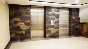 A modern elevator with metallic doors and a control panel, set in a hallway with dark patterned walls and a wooden railing. - Altabriza Resort Boracay (Boracay Island)