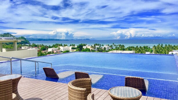 A pool with wicker furniture and a view of the ocean and buildings. - Altabriza Resort Boracay (Boracay Island)