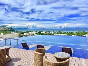 A pool with wicker furniture and a view of the ocean and buildings. - Altabriza Resort Boracay (Boracay Island)