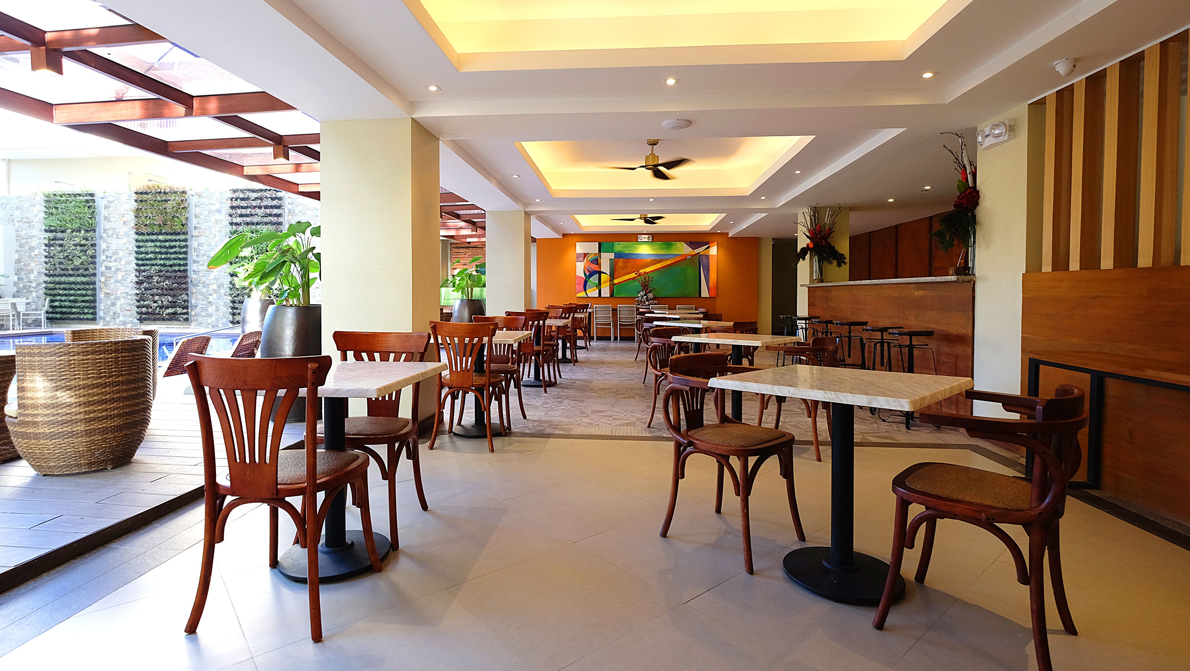 A spacious indoor dining area with multiple tables and chairs, a ceiling fan, and large windows allowing natural light.