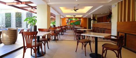 A spacious indoor dining area with multiple tables and chairs, a ceiling fan, and large windows allowing natural light.
