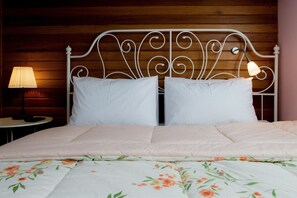 Una cama bien hecha con una colcha floral y almohadas blancas, una lámpara de noche y un cabecero de madera.