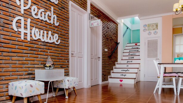 A room with a brick wall, a staircase with a sign reading "Every journey begins with just a single step," and a table with chairs. - Sweet Peach House (Senggigi)