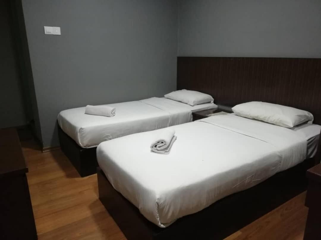 A room with two single beds, each with a white mattress and pillow, and a wooden headboard.