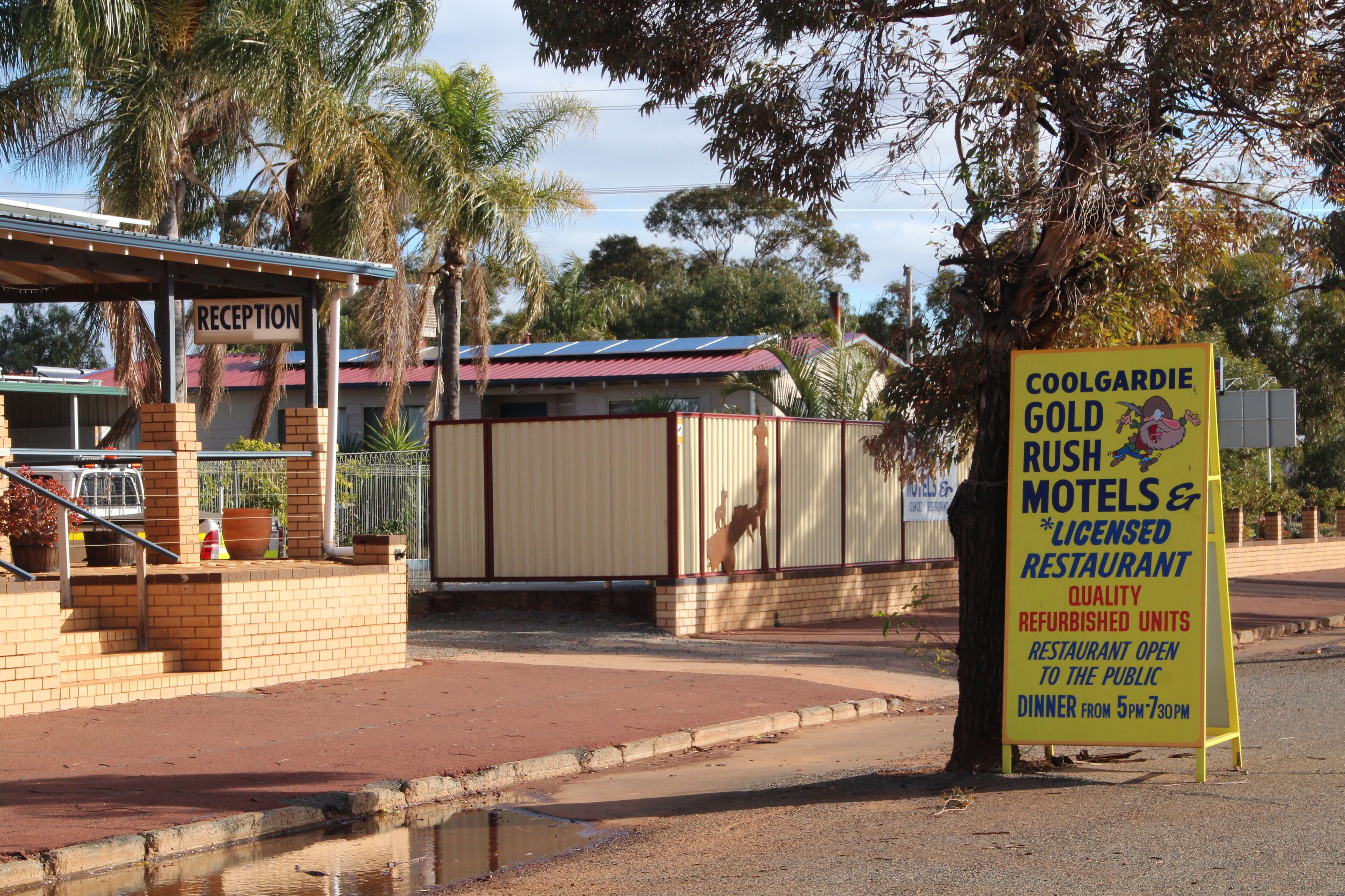 Un espace d’accueil avec une enseigne indiquant « Coolgardie Gold Rush Motels & Licensed Restaurant », signalant la rénovation des chambres et la possibilité de prendre des repas dans la salle à manger ouverte au public.