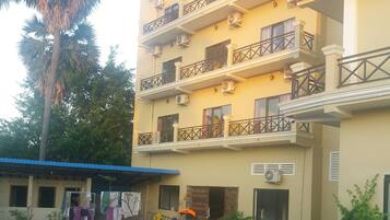 A multi-story building with balconies, a swimming pool, and a palm tree.