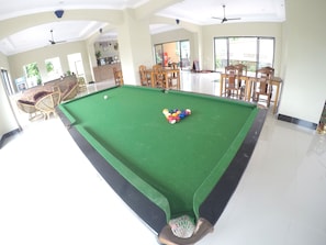 A pool table in a spacious room with natural light, wooden furniture, and a brick accent wall.