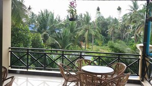 A balcony with a round table and wicker chairs, overlooking a lush garden with palm trees and a view of the surrounding landscape. - Blue Diamond Guest House - Hostel (Battambang)