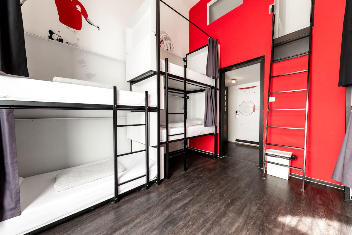 A dormitory room with bunk beds, a red accent wall, and a wooden floor.