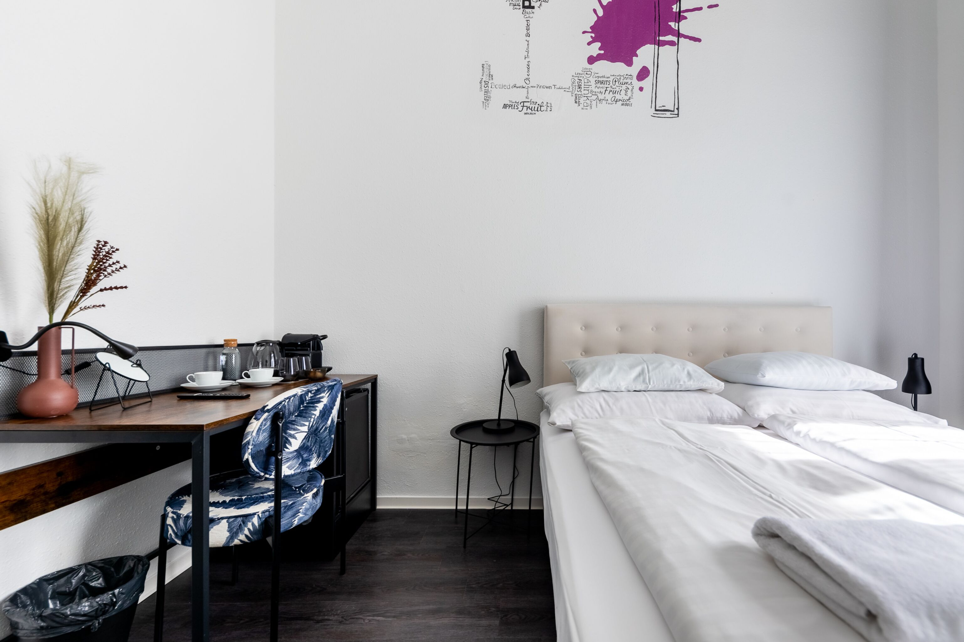 Une chambre à coucher moderne comprenant un lit, un bureau avec une chaise, une petite table et une œuvre d’art murale.