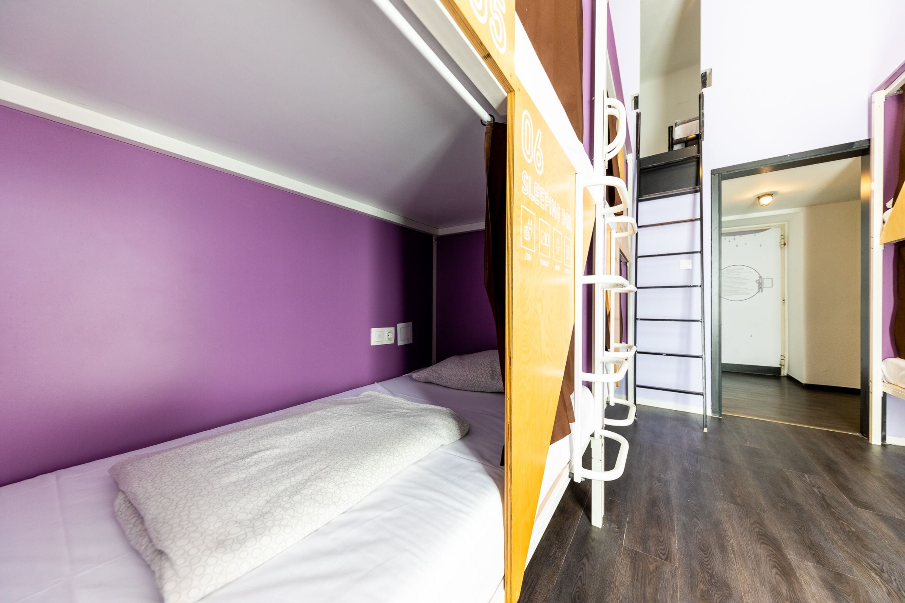 A room with purple walls, two beds with white bedding, a wooden ladder, and a door leading to another room.
