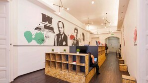A reception area with a wooden reception desk, a television, and a wall with artwork. - Adagio Hostel Basilica (Budapest)
