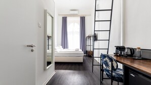 A compact hotel room with a bed, a desk with a chair, a ladder, and a coffee maker. - Adagio Hostel Basilica (Budapest)
