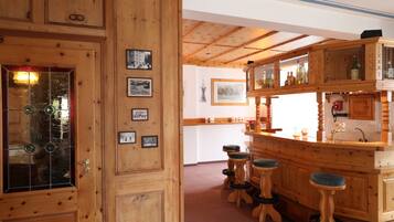 A wooden bar area with stools, a counter, and a door with glass panels and framed pictures.