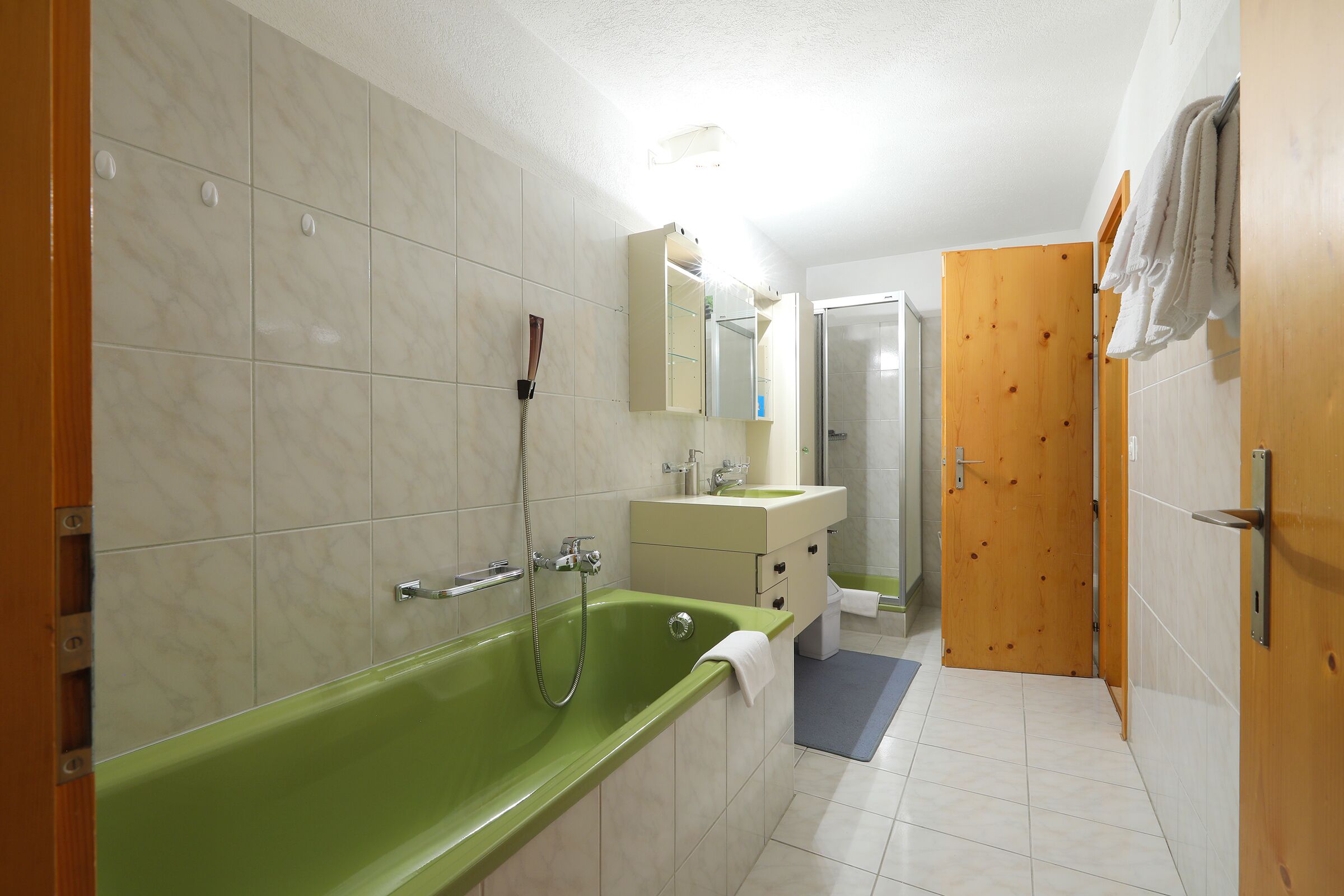 A bathroom with a green bathtub, a wooden door, and a white sink.