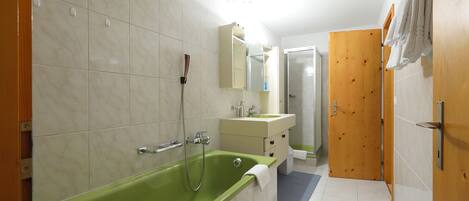 A bathroom with a green bathtub, a wooden door, and a white sink.