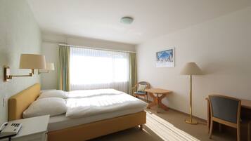 A hotel room with a bed, a desk with a phone, a chair, a small table, and a lamp.
