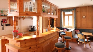A wooden bar area with a glass display case, wooden stools, and a seating area with a sofa and chairs. - Hotel Concordia Davos (Davos)