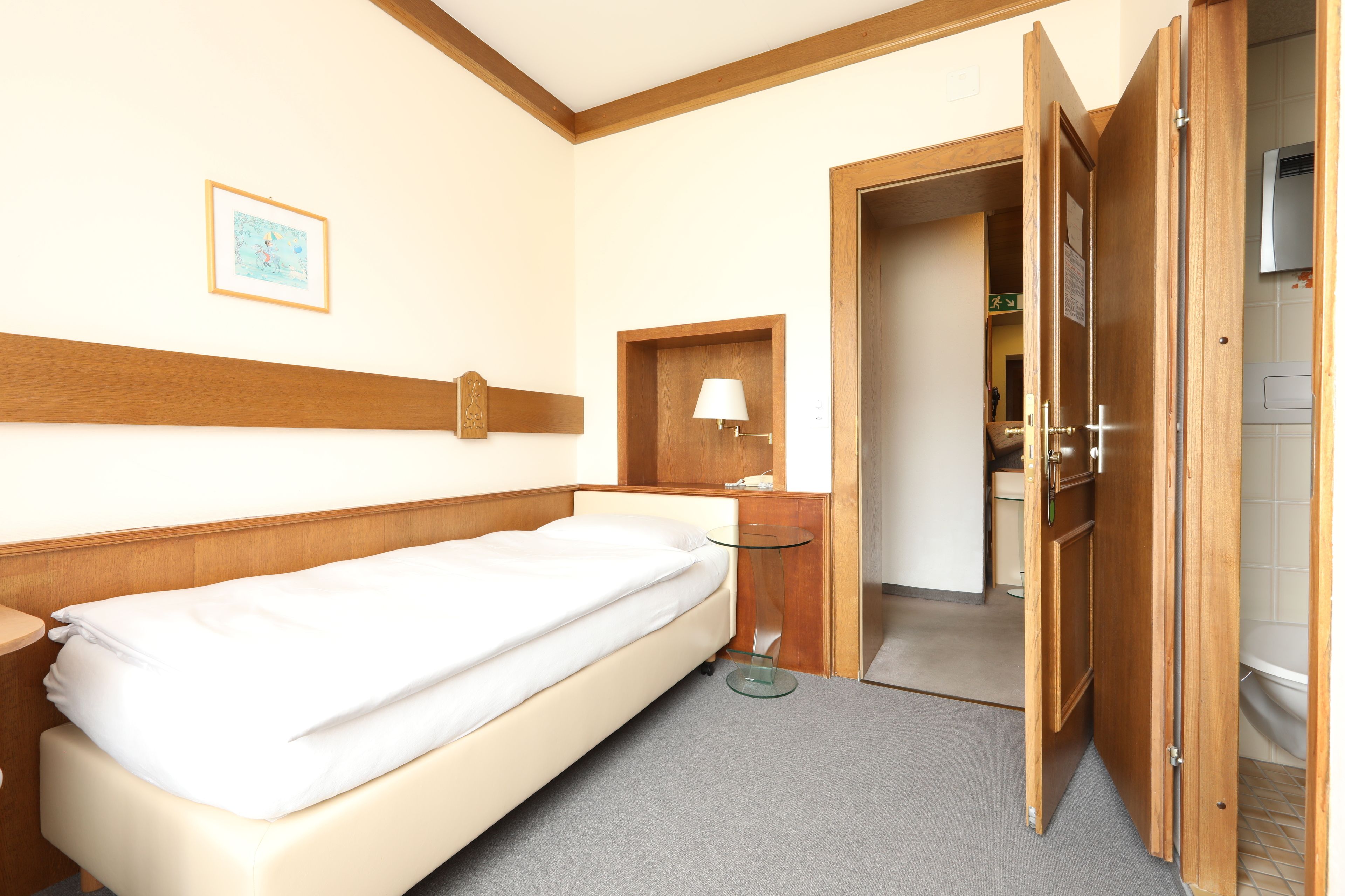 A single bed with a wooden headboard, a bedside table with a lamp, and a small framed picture on the wall.