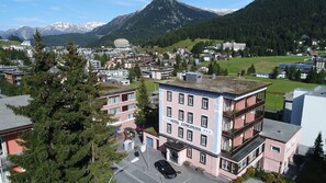 Un hotel de varios pisos con un letrero llamativo, rodeado por un pueblo con edificios y montañas al fondo.