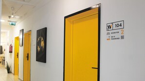 Un pasillo con puertas amarillas, una de ellas con un letrero que indica el número de habitación 104, acceso a Wi-Fi y un código QR.