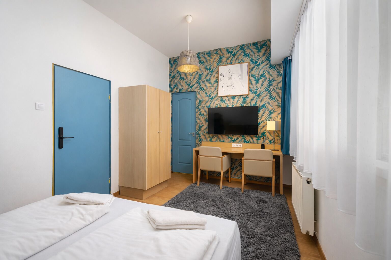 A bedroom with a bed, a desk with two chairs, a TV, and a wardrobe.