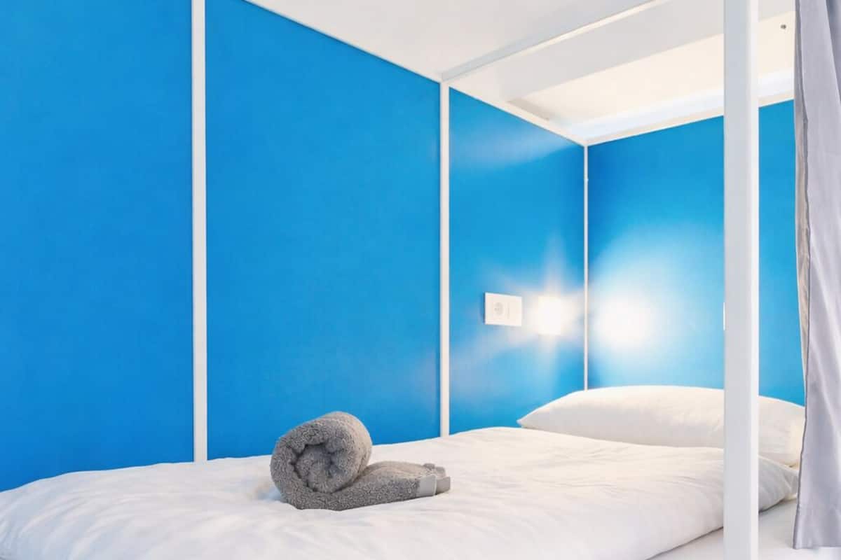 A bunk bed with a rolled towel on the lower bunk, white bedding, and a blue wall.